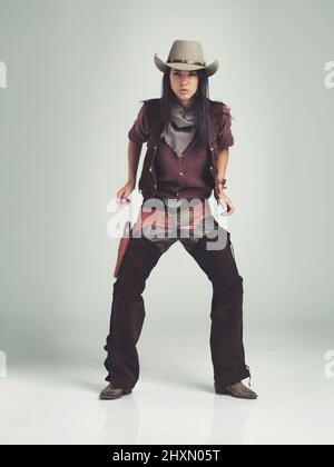 Im lo sceriffo intorno a queste parti.... Scatto a tutta lunghezza di una giovane donna attraente in abbigliamento cowboy. Foto Stock