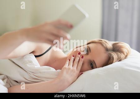 Controllare i feed dei social media. Scatto di una giovane donna attraente testando sul suo cellulare mentre si trova nel suo letto a casa. Foto Stock