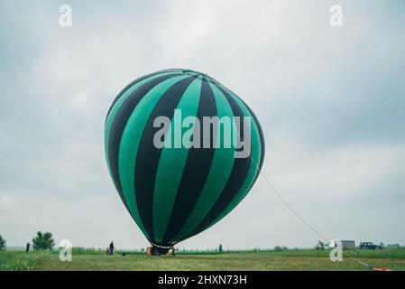 Gonfiando, disimballando e volando su l'anguria calda del mongolfiera. Bruciatore che dirige la fiamma nella busta. Decollare l'aereo volare nel cielo blu del mattino. Avviare la combustione ad aria calda per gonfiare il gas al palloncino. Foto Stock