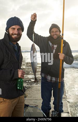 Stanotte mangiavano pesce. Shot di due giovani uomini che pescano fuori da un molo con un pesce su una linea. Foto Stock