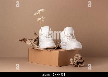 Scarpe ecologiche in pelle. Un paio di sneaker beige con fiori secchi su sfondo marrone. Stile di vita sportivo informale. Foto Stock