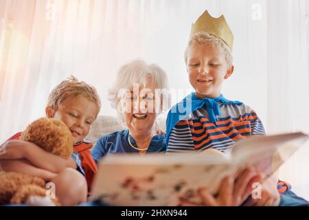 Granny sta leggendo di nuovo la nostra storia preferita. Colpo di una donna anziana che trascorre il tempo a sguastare i suoi nipoti. Foto Stock