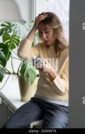Depressi in mezza età donna tiene smartphone leggere spiacevoli sms ricezione di cattive notizie a casa. Foto Stock