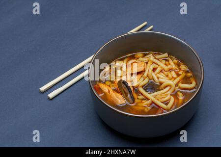 Zuppa Tom Yam con salmone e verdure come ciliegie, peperoncino, erba limone su sfondo grigio Foto Stock