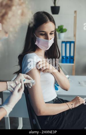 Ritratto di infermiere professionista in maschera medica e guanti che danno l'iniezione di influenza alla donna che guarda in giù caucasica. Protezione da virus. Dottore che dà Foto Stock