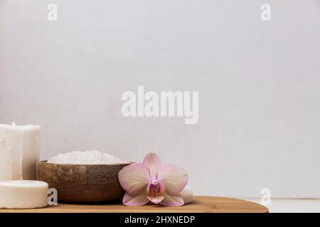 Preparazione per il trattamento spa dell'hotel, procedura per il bagno in casa. Lavabo grigio in bagno, accessori su vassoio di legno candela Burning, sale marino in ciotola di bambù, fiore di orchidea, sapone ecologico fatto in casa Foto Stock