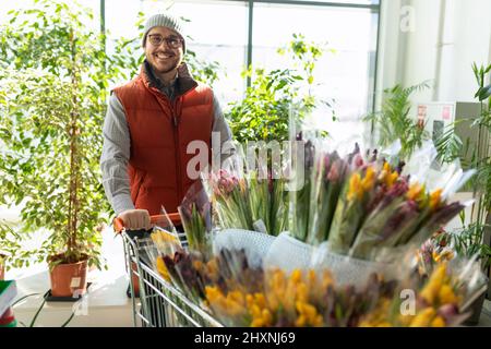 un dipendente di un negozio di piante da giardino e fiori porta un carrello con mazzi di tulipani Foto Stock