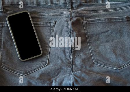 La parte superiore dei vecchi jeans neri indossati e uno smartphone con schermo nero Foto Stock