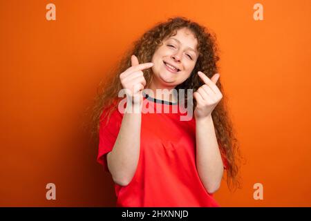 Gioiosa bella donna rossa in t-shirt rossa mantenendo le dita incrociate come una fortuna per la squadra di calcio nel campionato. Foto Stock