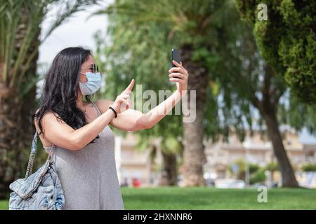 Donna adulta che prende un selfie e che fa segno di pace nel parco Foto Stock