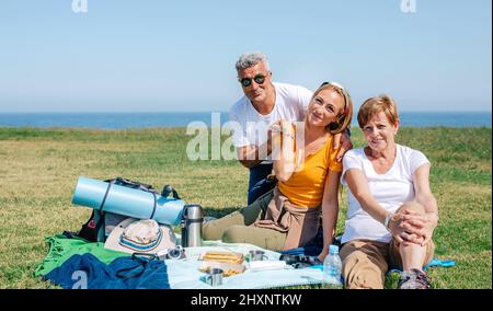 Famiglia adulta che guarda la macchina fotografica seduta su una coperta per fare un picnic Foto Stock