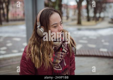 Giovane donna felice con sindrome di Down ascoltare la musica in città in inverno Foto Stock