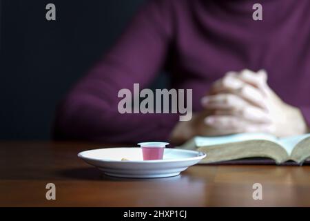 Vino e pane della Santa comunione con le mani della donna in una postura di preghiera in cima alla bibbia aperta sullo sfondo. Foto Stock