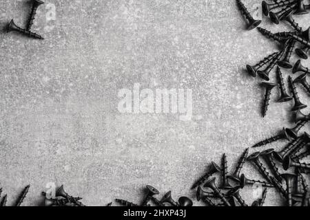 Componenti di costruzione. Viti autofilettanti nere su fondo grigio calcestruzzo. Spazio di copia. Vista dall'alto Foto Stock