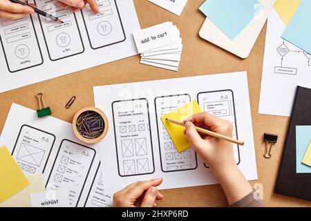 Due web designer che lavorano insieme su un sito web mobile reattivo. Immagine piatta di numerosi schizzi di strutture a reticolo di app sulla scrivania dei progettisti di prodotti. Foto Stock