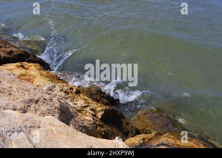 Piccole onde che colpiscono rocce bagnate al mare in una giornata di sole Foto Stock