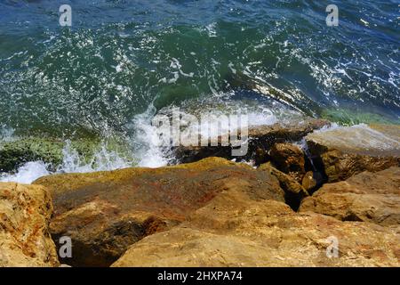 Piccole onde che colpiscono rocce bagnate al mare in una giornata di sole Foto Stock