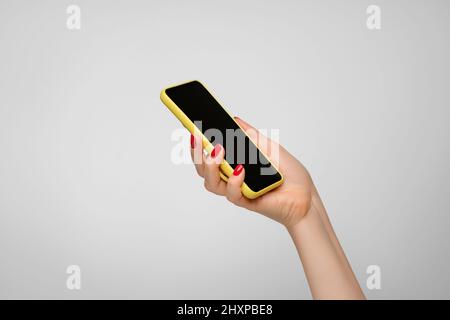 Telefono cellulare con cassa giallo brillante in mano di una donna con unghie rosse. Foto Stock