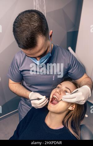 Paziente in studio dentistico. Giovane donna seduta sulla sedia in studio dentistico e medico che esamina i denti Foto Stock