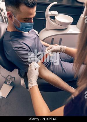 L'infermiere applica un laccio emostatico su un braccio del paziente prima di prelevare il sangue Foto Stock