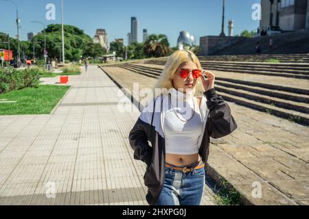 Bella giovane Latina in una maglietta bianca che cammina lungo il marciapiede in un parco pubblico. Concetto di donna moderna. Foto Stock