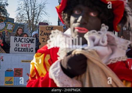 Molte persone travestite da Zwarte Piet passano di fronte alla dimostrazione del gruppo anti-razzista a Zaandam Foto Stock