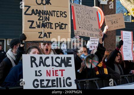 Molte persone travestite da Zwarte Piet passano di fronte alla dimostrazione del gruppo anti-razzista a Zaandam Foto Stock