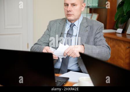 Uomo d'affari anziano seduto alla tavola rotonda e documento di strappo Foto Stock