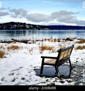 Una panchina parco vuota in una giornata d'inverno con una vista sull'oceano di un'isola lontana. Foto Stock