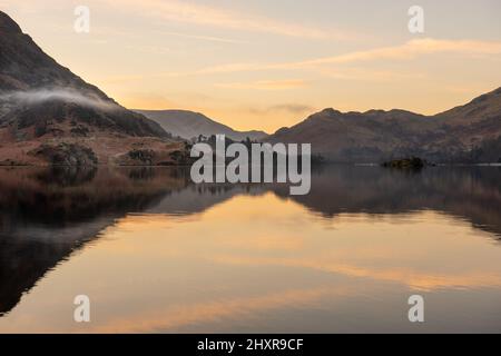 Un'alba tranquilla al lago con riflessi calmi in una bella mattinata estiva. La nebbia ondulata si può vedere che si aggira intorno alle montagne. Cumbria. Foto Stock