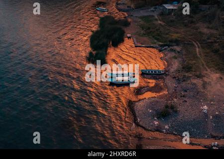 Vista dall'alto delle barche ormeggiate sulla costa rocciosa del blu lago Atitlan in Guatemala al tramonto Foto Stock