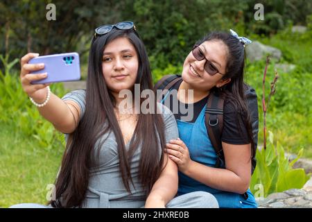 Scatto di due ragazze che siedono in un parco e prendono selfie con il telefono Foto Stock