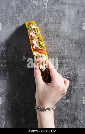 tacos di mais con salmone, maionese e pistacchi su un tavolo di cemento e una mano femminile Foto Stock