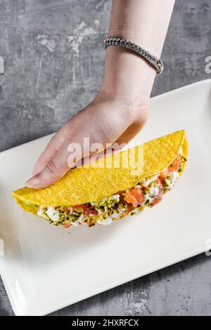tacos di mais con salmone, maionese e pistacchi su un tavolo di cemento e una mano femminile Foto Stock