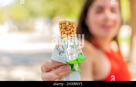 Primo piano di una mano femminile che tiene una barra di cereali pronta a mangiare in un parco Foto Stock