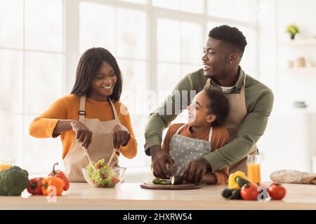 I genitori neri e la figlia cucinare preparare insalata di verdure in cucina Foto Stock