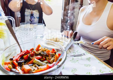 primo piano di una ciotola di vetro con verdure fritte mescolate sul tavolo con persone sfocate sullo sfondo, ripieno per arepa per il pranzo. Foto Stock