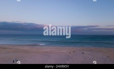 Tramonto sulla spiaggia con sci e oceano blu sullo sfondo visto dall'alto. Concetto di bel paesaggio costiero e la gente che cammina sulla sabbia. Foto Stock