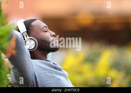 Ritratto laterale di un uomo con pelle nera rilassante ascolto di musica con le cuffie in un parco Foto Stock