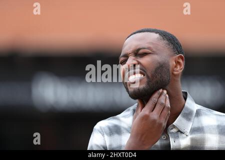 Uomo con pelle nera che soffre mal di gola lamentandosi per strada Foto Stock