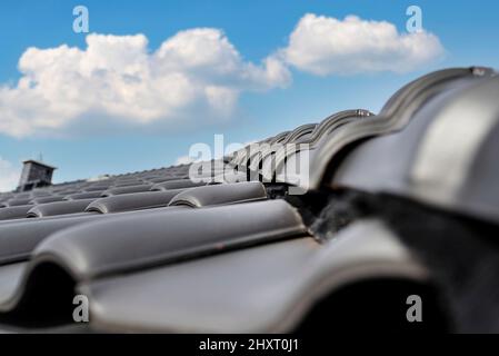 Tegola di cresta sul tetto di una casa singola-familiare coperta con una nuova piastrella in ceramica in antracite contro il cielo blu. Foto Stock