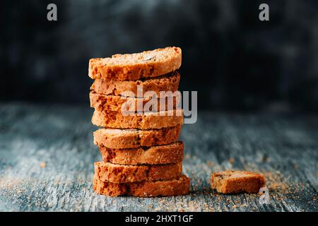 primo piano di una pila di carquinioli, biscotti di mandorle tipici della catalogna, spagna, su un tavolo grigio rustico in legno, di fronte ad un chiazzetto grigio scuro Foto Stock