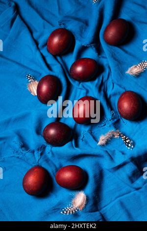 Belle uova di borgogna con piume su tessuto blu. Concetto di Pasqua in stile rustico Foto Stock