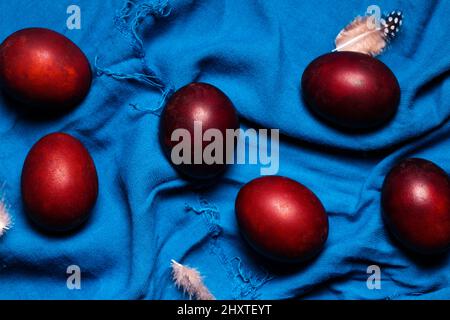 Belle uova di borgogna con piume su tessuto blu. Concetto di Pasqua in stile rustico Foto Stock