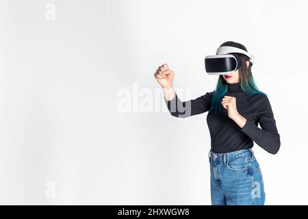 Ragazza adolescente che usa la punzonatura del visore vr, lotta con qualcuno nello spazio di gioco, realtà virtuale su sfondo bianco, spazio di copia. Giochi di combattimento virtuale. Foto Stock