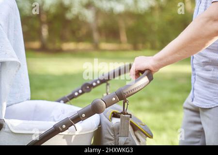 Un giovane papà che cammina nel parco con un bambino in un passeggino. Primo piano delle mani degli uomini con un passeggino. Concetto di Father's Day. Foto di alta qualità Foto Stock