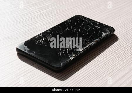 Smartphone nero con display rotto su superficie di legno. Riparazione dello smartphone. Sostituzione del display dello smartphone. Foto Stock