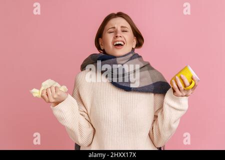 Ritratto di infelice donna bionda disperata malsana che è avvolta in sciarpa che soffre di influenza, fells cattivo, prendere freddo, naso che cola, indossare maglione bianco. Studio interno girato isolato su sfondo rosa. Foto Stock