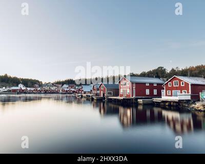 Splendida vista sulle case di legno rosso vicino ad un lago con riflessi nell'acqua a Bonhamn, Svezia Foto Stock