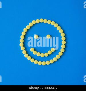 Faccia sorridente da pillole rotonde gialle su sfondo blu. Compresse, pillole, vitamine, concetto di medicina. Foto Stock
